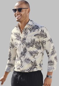 Korte mouwen overhemd in lichtbeige met een zwart palmbladpatroon. Voorzien van een kraag, knoopsluiting en een borstzak aan de linkerzijde. Gepaarde met zwarte shorts.