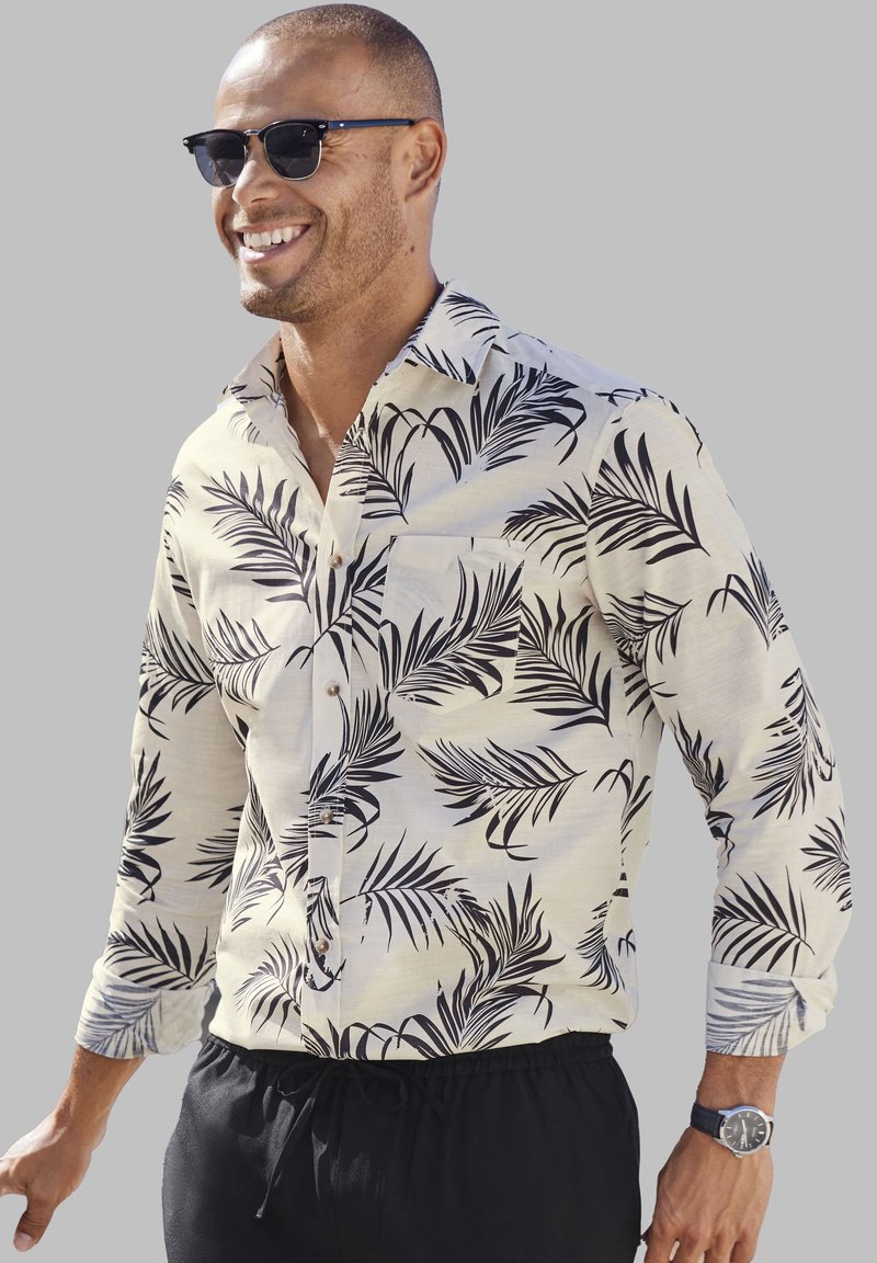 Korte mouwen overhemd in lichtbeige met een zwart palmbladpatroon. Voorzien van een kraag, knoopsluiting en een borstzak aan de linkerzijde. Gepaarde met zwarte shorts.