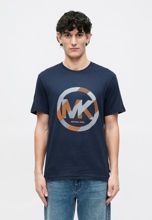 Tamsiai mėlynas medvilninis marškinėliai su apvaliu, dryžuotu oranžiniu ir baltu "MK" logotipu, po kuriuo išdėstyta tekstas "MICHAEL KORS".