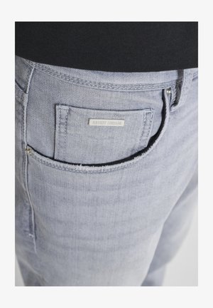 Lichtblauwe spijkerbroekzak met een klein metalen label met de naam "ANTONY MORATO" op een persoon die een zwart topje draagt.