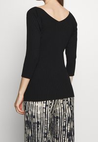 Suéter negro de canalé con escote en V, mangas largas, diseño ajustado y tejido texturizado. Combinado con pantalones de pierna ancha con estampado.