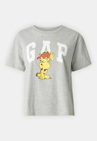 Camiseta de algodón gris con un gran logo blanco de "GAP" y un gato de dibujos animados con gafas de sol rojas. Mangas cortas y un ajuste relajado.