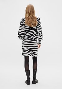 Musta-valkoraidallinen neulemekko pitkillä hihoilla, joka ulottuu reiden puoliväliin, yhdistettynä mustiin polveen yltäviin saappaisiin ja läpinäkyviin mustiin sukkahousuihin.