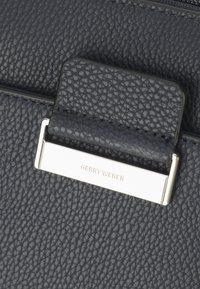 Borsa a mano in pelle blu scuro con finitura testurizzata. Presenta una placca logo argentata con "GERRY WEBER" e un accento hardware rettangolare liscio.