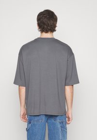 Camiseta gris de gran tamaño hecha de una suave mezcla de algodón, con mangas cortas, un cuello redondo y un dobladillo recto. La tela tiene una textura lisa.