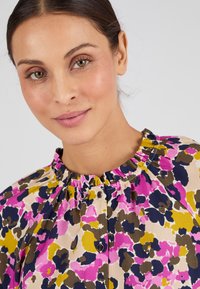Blusa floreale con scollatura arricciata, caratterizzata da colori rosa, viola, verde e navy in un tessuto morbido. Dettaglio con bottoni sul davanti.