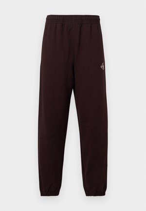 Mörkbruna sweatpants med resårmidja, avsmalnande ben och en liten gulddetalj med logga på vänstra sidan. Mjuk tygtextur.