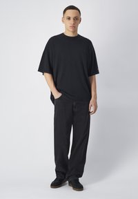 Zwarte oversized t-shirt, korte mouwen, ronde hals; gecombineerd met zwarte loszittende jeans en donkere sneakers. Eenvoudig, effen kleur zonder patronen.