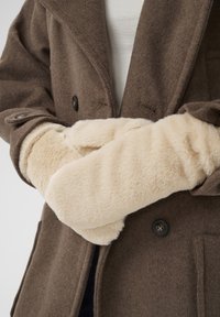 Cămașă de lână maro cu mănuși mari din artificial de blană crem. Mănușile sunt pufoase, texturate și acoperă complet mâinile. Detaliu notabil cu nasturi negri vizibili.