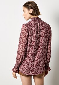 Blusa bordeaux con un motivo paisley floreale, maniche lunghe con polsini arricciati e scollo arricciato, realizzata in tessuto leggero.