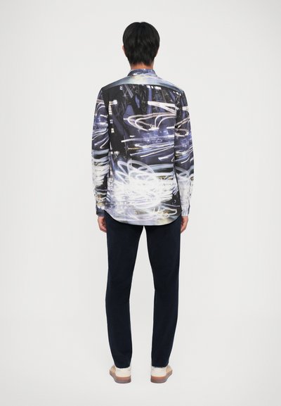 Langermige shirt met abstracte blauwe en witte patronen, ontworpen in lichtgewicht stof. Gepaard met donkere broek en beige schoenen.