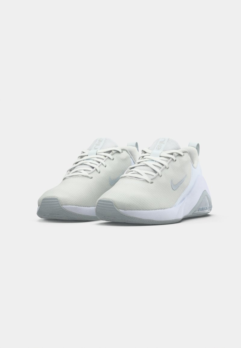 Lys grå træningssko med et åndbart mesh-overdel, hvide detaljer, rund tå og struktureret sål med et Nike-logo.