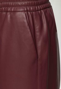 Bordó kožená sukně s elastickým pasem a boční kapsou, vyznačující se detailní texturou a prošitím.