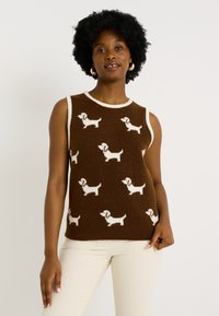 Pull sans manches marron avec des motifs de teckels crème, texture tricotée, et un col rond côtelé blanc. Porté sur un pantalon clair.