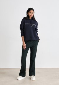 Granatowy hoodie z białym napisem "TOMMY HILFIGER", zestawiony z ciemnozielonymi spodniami i białymi trampkami na platformie. Gładki materiał, luźny krój.