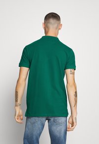 Polo vert avec un col, à manches courtes et à ourlet droit. Le tissu semble lisse, avec des détails de couture visibles.
