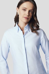 Jasnoniebieska, długorasowa koszula zapinana na guziki z wyrazistym kołnierzykiem, charakteryzująca się dopasowanym krojem i gładką teksturą. Widoczne klasyczne białe guziki.