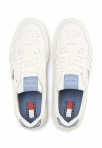 Zapatillas de cuero blancas con detalles perforados, plantillas azules y una etiqueta en la lengüeta azul con acentos de marca en rojo, blanco y azul.