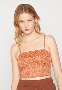 Crop top orange et marron avec un motif ondulé, fines bretelles et encolure carrée. Fabriqué en tissu léger avec une texture lisse.