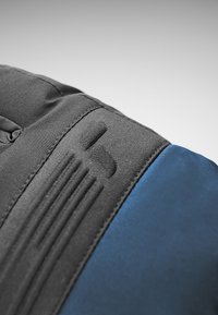 Svart tygsektion med texturerade accenter och en blå sektion. Inkluderar en upphöjd logotyp och sömdetaljer längs s�ömmarna.