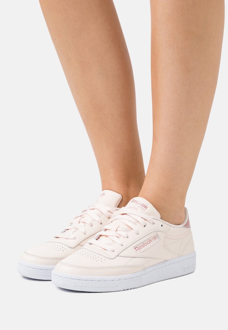 Light pink Reebok sneakers with a smooth leather upper, white rubber sole, round toe, and lace-up design featuring perforated detailing.