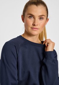 Sudadera azul marino con cuello redondo acanalado, mangas tipo raglán y textura suave. Detalles de costura visibles y un ajuste relajado.