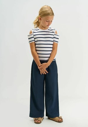 Top a maniche corte a righe bianche e blu navy, con spalle scoperte, abbinato a pantaloni blu navy a gamba larga e sandali marroni.