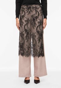 Pantalon à superposition de dentelle noire avec des motifs floraux complexes, associé à un pantalon large couleur beige clair. Doté d'une taille ajustée et d'un design texturé.