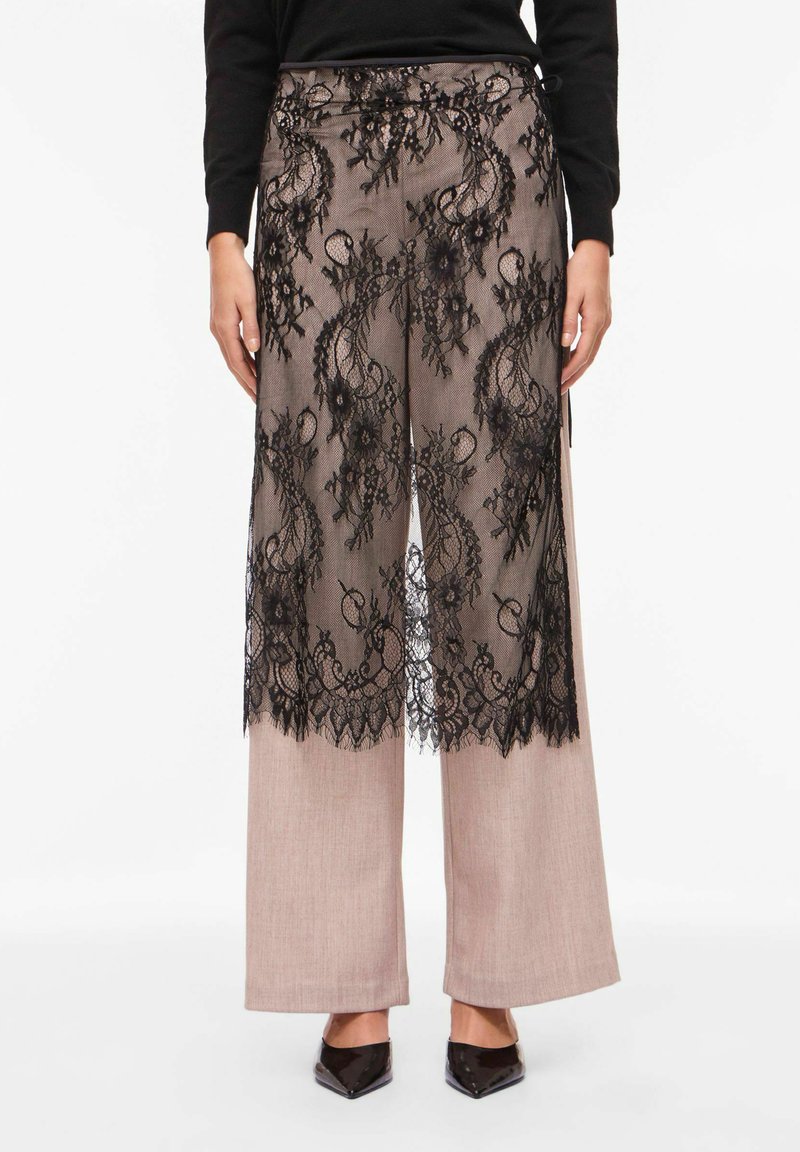 Pantalon à superposition de dentelle noire avec des motifs floraux complexes, associé à un pantalon large couleur beige clair. Doté d'une taille ajustée et d'un design texturé.