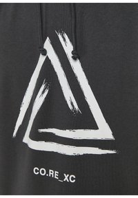 Sudadera negra con un gran gráfico triangular en trazo blanco y el texto “CO.RE_XC” debajo. Los cordones son visibles en el cuello.