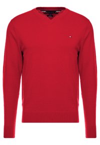 Punainen pitkähihaisuus V-pääntie neulepusero, jossa pieni brodeerattu logo vasemmassa rinnassa, ribattu hihansuu ja helma.
