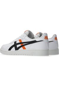 White leather sneakers with black and orange accents, featuring a textured upper, lace-up design, and a flexible rubber sole.