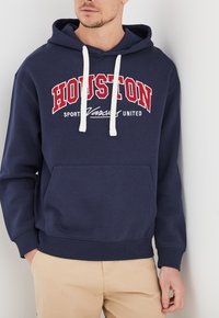 Felpa blu navy realizzata in morbido tessuto, con la scritta "HOUSTON" in rosso sul petto, cordini bianchi e una tasca frontale.