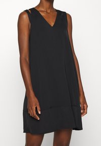 Vestido negro sin mangas con escote en V, silueta fluida y diseño minimalista. Presenta tirantes y dobladillo recto. Textura de tela suave.