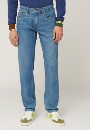 Jeans in denim blu chiaro con vestibilità rilassata, caratterizzati da dettagli cuciti, passanti per cintura e tasche frontali, abbinati a sneakers bianche e verdi.