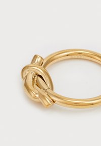 Gold ring featuring a knot design, smooth finish, circular shape, and a small band detail where the knot connects.