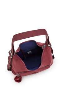 Maroon Kipling axelväska med justerbar rem, öppen dragkedja som visar en mörkblå insida och en liten fäst plushnyckelring.