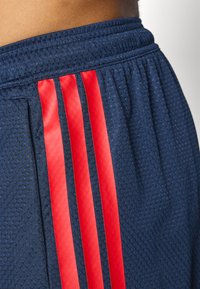 Marineblauwe sportshorts met een tekstuurpatroon, voorzien van drie verticale rode strepen aan de zijkant. Elastische tailleband voor comfort.