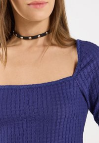Top viola a coste con scollatura quadrata, con rifiniture in pizzo. Accompagnato da un choker nero con borchie argentate.