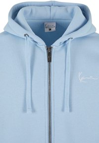 Hellblaues Zip-Hoodie aus weichem Stoff. Verfügt über eine Kapuze mit Kordelzug, einen silbernen Reißverschluss und ein dezentes, weißes, gesticktes Logo.