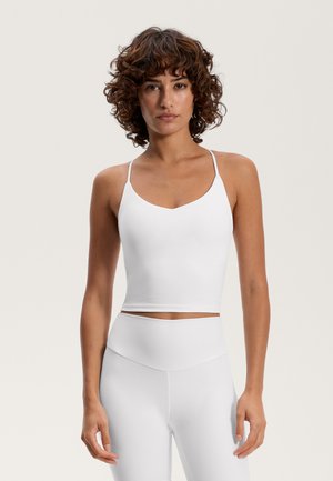 Weißes, kurzes Tanktop mit dünnen, verstellbaren Trägern; glatter, elastischer Stoff; kombiniert mit hochgeschnittenen weißen Leggings. Einfaches Design.