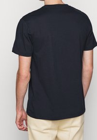 Černé bavlněné tričko s krátkými rukávy a kulatým výstřihem, pohled zezadu. Hladká textura, žádné viditelné vzory nebo grafika.