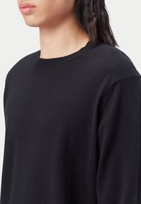 Schwarzer Pullover mit Rundhalsausschnitt. Verfügt über eine weiche Textur und ein schlichtes Design. Keine Muster oder Akzente sichtbar.