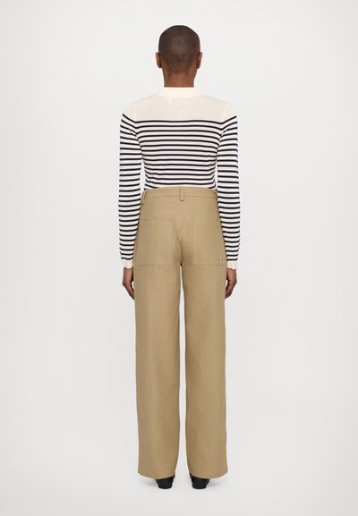Maglietta a maniche lunghe a righe in crema e navy, abbinata a pantaloni larghi beige con due tasche posteriori, mostrata da dietro.