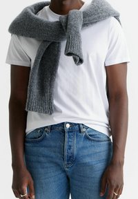 Bufanda gris de punto drapeada sobre una camiseta blanca, combinada con jeans azules. La bufanda tiene una textura acanalada y está hecha de un material suave y esponjoso.