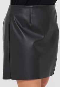 Mini falda de cuero negro con una textura suave, que presenta un ligero brillo, una costura trasera y un corte recto sin adornos.