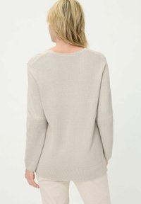 Lichtbeige gebreide trui met een gestructureerd patroon, lange mouwen en een ronde hals. Heeft een relaxte pasvorm en een geribde zoom.