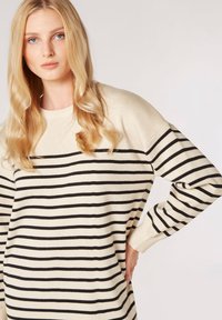 Beige Strickpullover mit horizontalen schwarzen Streifen, lässiger Schnitt, weiten Ärmeln und Rundhalsausschnitt. Glatte Textur mit minimalen Details.