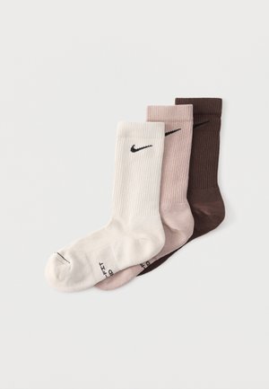 Three ribbed crew socks in white, light pink, and dark brown, each featuring a black Nike swoosh near the cuff.