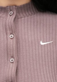 Μακρυμάνικη, μώβ ριμπ βαμβακερή μπλούζα με ψηλό γιακά, διαθέτει τέσσερα κουμπώματα και λευκό λογότυπο Nike στην αριστερή πλευρά.